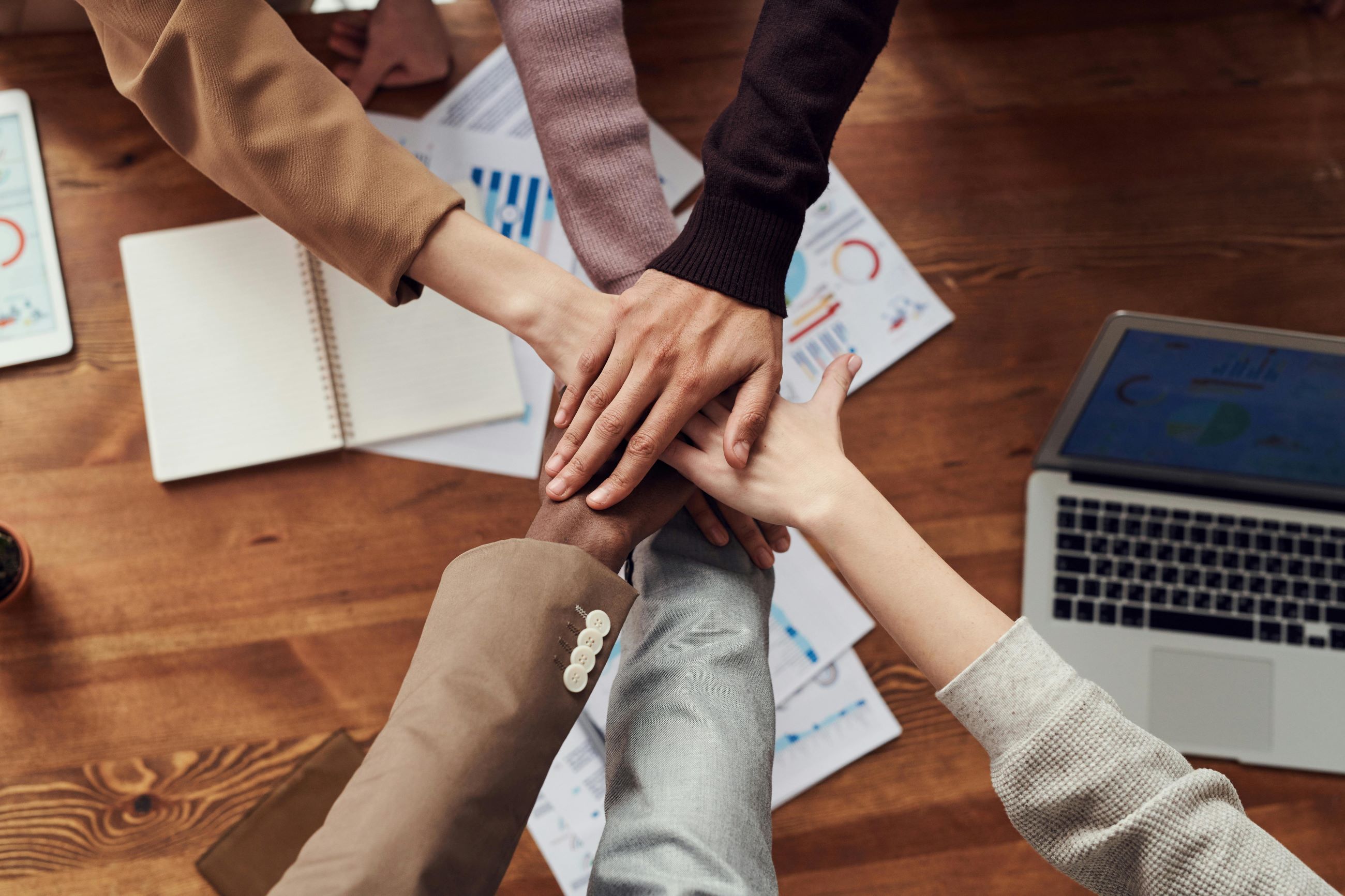 Team members stack hands above project meeting table