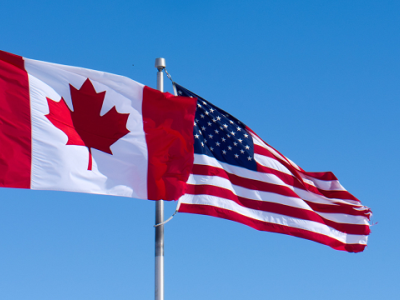 the Canada and U.S. flags flying against a blue sky