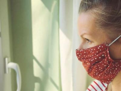 woman in mask looking out the window